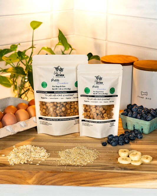 Two bags of Lili & Astara pet food on a wooden table with ingredients and a plant in the background.