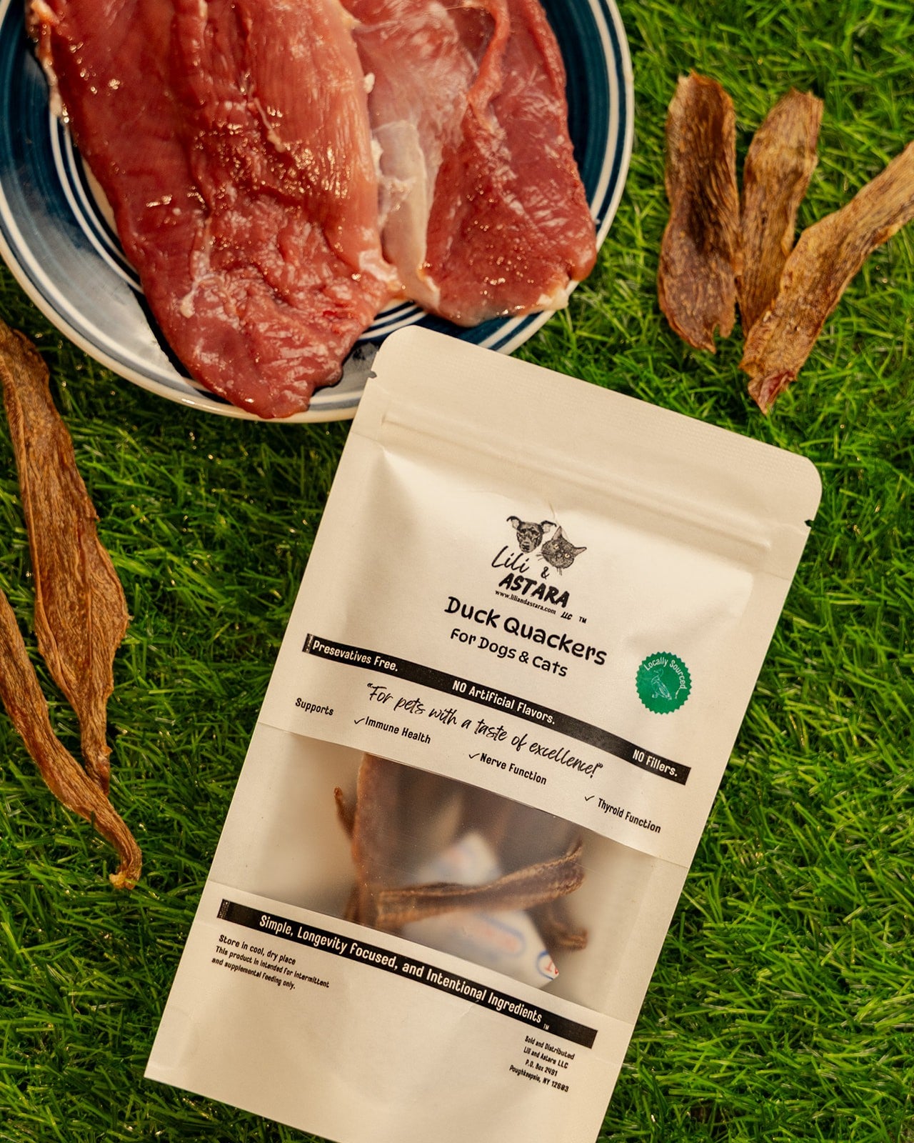 Package of Duck Quackers pet treats on grass with raw duck meat in the background